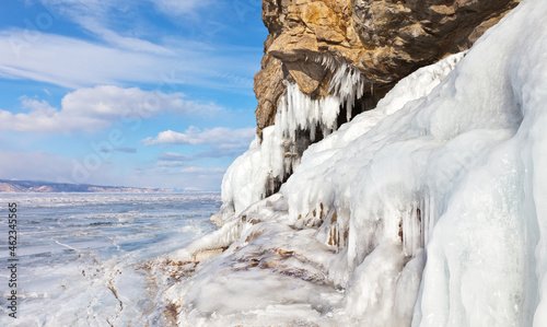 A sunny day of early spring on the frozen Baikal Lake. The ice crust on the cliffs of Olkhon Island begins to melt in the bright sun. March is a great time for ice travel and hike