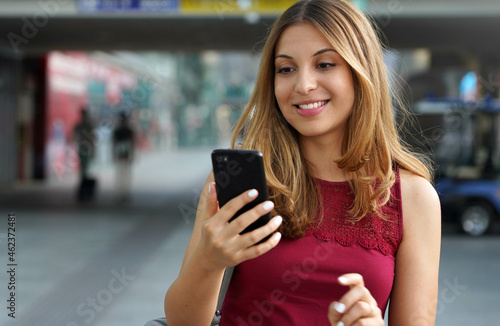 Close-up of charming beautiful business woman smile in casual style using smartphone walking in train or metro station. Copy space.