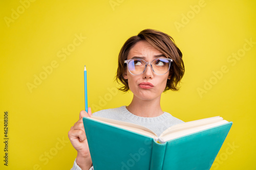 Photo of smart lady read book hold pencil look empty space wear specs blue pullover isolated yellow color background