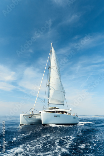Luxury catamaran sailing under white sails on the blue azure sea on a sunny summer day. Travel, yachting, regattas concept