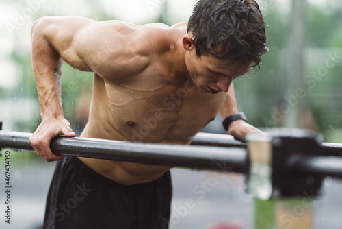 Shirtless sportsman doing exercise on uneven bars at playground