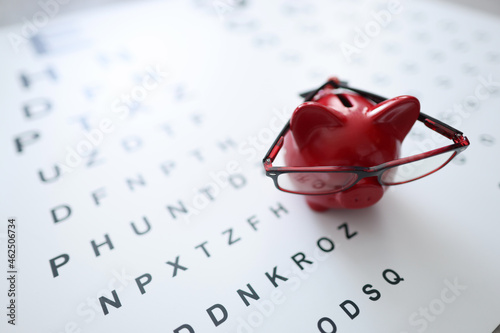 Red pig piggy bank in glasses stands on ophthalmological table closeup