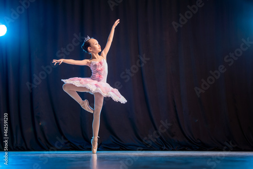 little girl ballerina is dancing on stage in white tutu on pointe shoes classic variation.