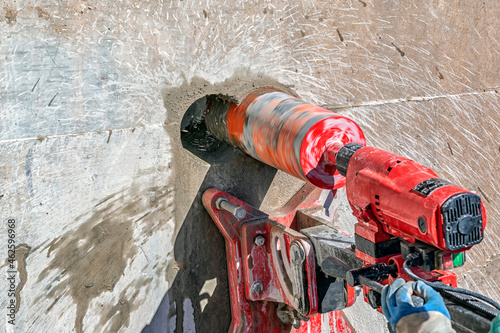 Worker is drilling to concrete wall with core drill machine. Core drills used in metal are called annular cutters. Core drills used for concrete and hard rock generally use industrial diamond grit.