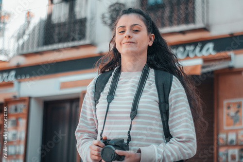 Mujer convencida joven veraneante trotamundos realizando fotos en la ciudad con su cámara para una sesión de fotografías de su viaje por España junto con su equipaje y mochila 