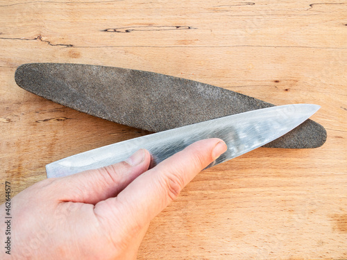 hand sharpens kitchen knife closeup on whetstone