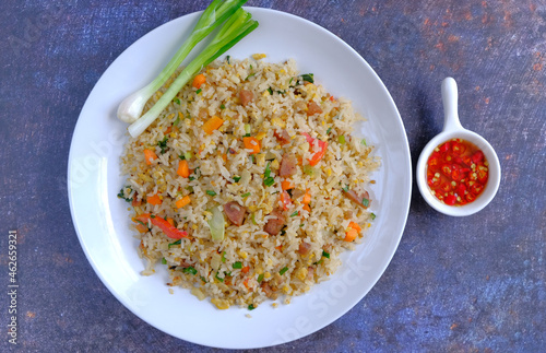 fried rice with spring onions on the white plate and sauce chili on a black background 