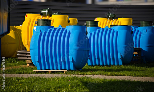 Plastikowe zbiorniki do przydomowych oczyszczalni ścieków . Żółty , niebieski . Beczka, metalowy płot . Plastic tanks for home sewage treatment plants. Yellow, blue. Barrel, metal fence. 