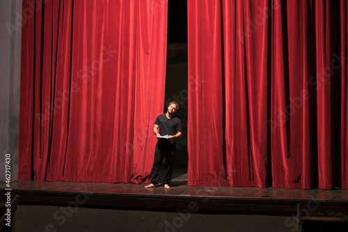 Barefoot actor with script standing on theatre stage