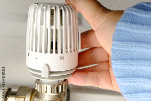woman regulates the temperature in the house with a thermostat on the white radiator, close-up female hand, concept of saving heat, the beginning of the heating season, shallow depth of field focus