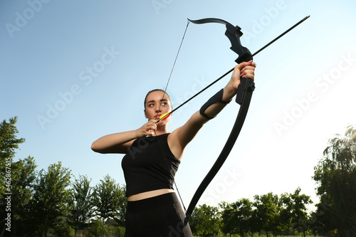Woman with bow and arrow practicing archery outdoors, low angle view