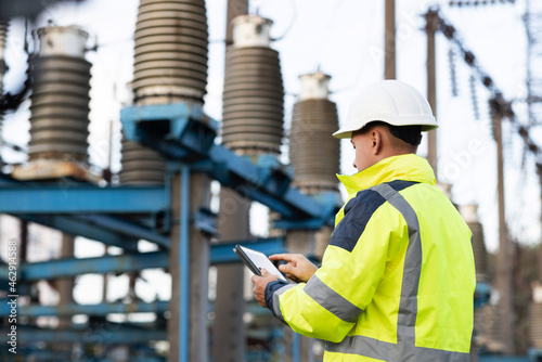 Electrical engineer studying reading on tablet. Electrical worker engineer a working with digital tablet, power near tower with electricity. Energy business technology industry concept