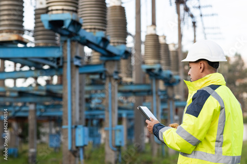 Energy business technology industry concept. Electrical engineer studying reading on tablet. Electrical worker engineer working with digital tablet near tower with electricity