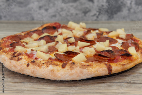 Freshly baked pineapple and pepperoni pizza with chopped vegetable toppings served on a wooden platter