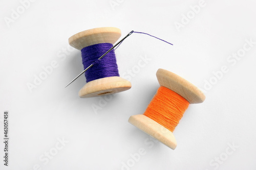 Colorful sewing threads with needle on white background, top view
