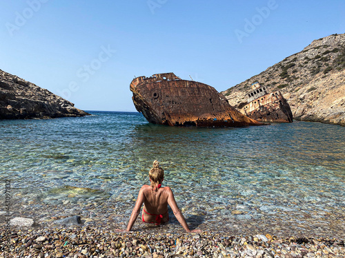 Back view on a woman wearing a red bikini looking at Shipwreck Olympia boat in Amorgos island during summer holidays, Cyclades, Greece. Travel background
