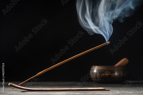 Asian incense stick in stick holder burning with smoke on black background