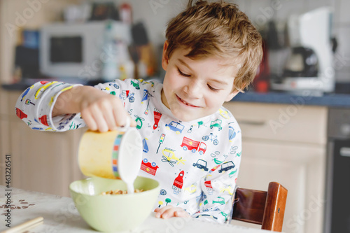 Happy little blond kid boy eating cereals for breakfast or lunch. Healthy eating for children in the morning. Child in colorful pajama nightwear having breakfast with milk and oat granola muesli