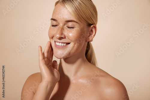 Cheerful female with blond hair massaging her cheek in studio against pastel background