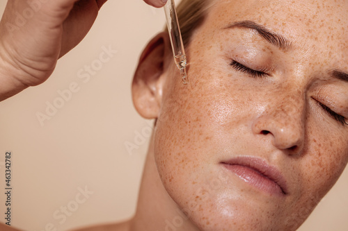 Young beautiful woman with closed eyes applying face serum with pipette