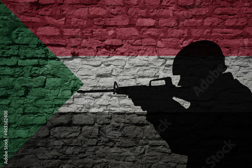 Soldier silhouette on the old brick wall with flag of sudan country.