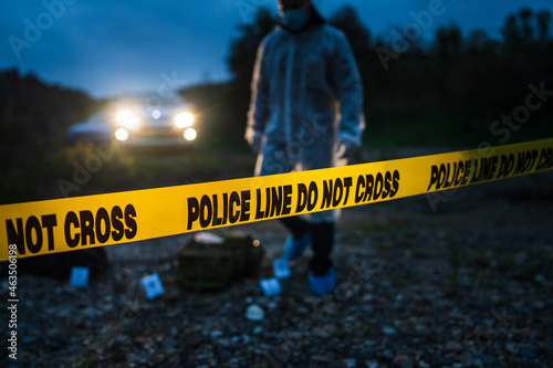 Forensic police investigator collecting evidence at the crime scene by the river in nature at night selective focus on police line tape