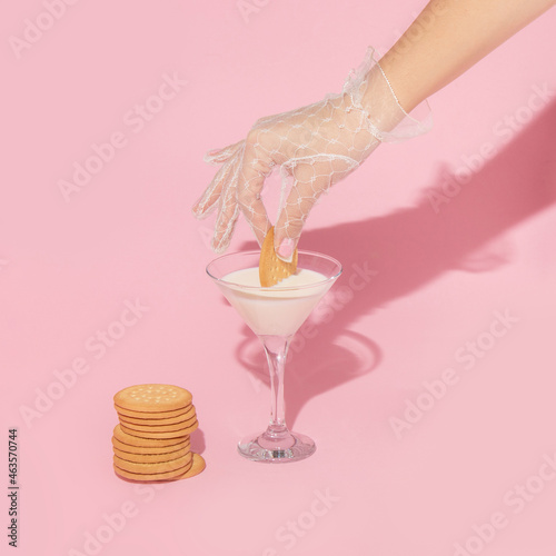 Creative layout with hand in white lace glove dipping cookie in milk in martini cocktail glass. 80s or 90s retro aesthetic fashion concept. Romantic valentines day drink idea.