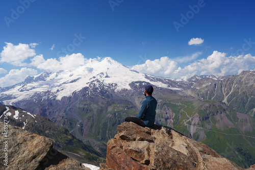 A man sitting on a brown stone ledge amid distant mountain peaks