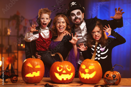 Young caucasian family mother father and children in Halloween costumes and makeup making scary gesture, saying trick or treat while celebrating together all hallows eve in dark room at home