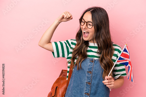 Young caucasian student woman studying English isolated on pink background raising fist after a victory, winner concept.