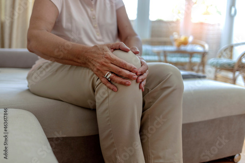 Old senior adult woman female hands touching knee sitting alone. Retired elderly grandma feeling hurt joint pain in leg suffering from osteoarthritis bones disease or injury concept, close up.