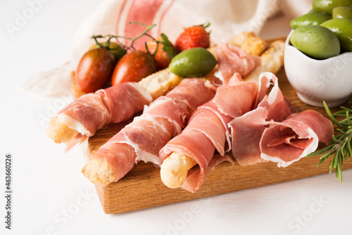 Traditional Italian wine appetizer - breadsticks grissini, prosciutto, jamon, olives and strawberries, close up