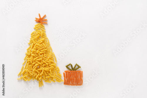 Alternative Christmas tree of dry pasta coloful fusilli with gift on white background. Merry Xmas greeting card with copy space. View from above. Food holiday concept. DIY for child.