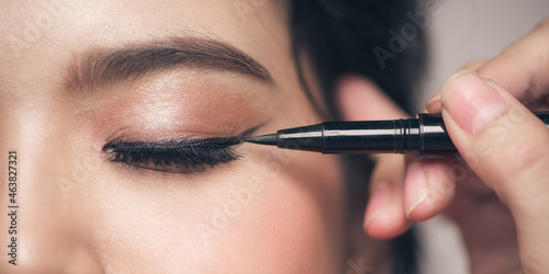 Make-up artist brush black eyeliner on the face of the woman.