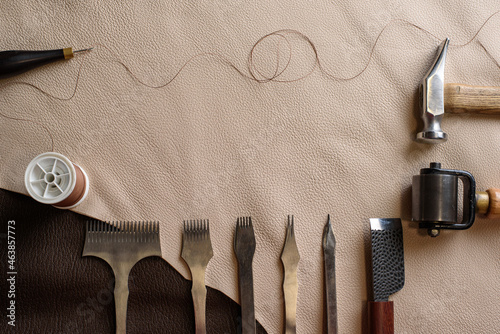 Shoemaking tools for sewing handmade shoes in workshop. Punches, awl, hammer, thread, roller on genuine leather. Workplace of shoemaker. Copy space.