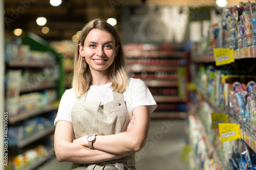 portrait of saleswoman, woman smiling and looking at camera in supermarket. Pleasant friendly female seller standing in the store between the rows . Trade business and people concept