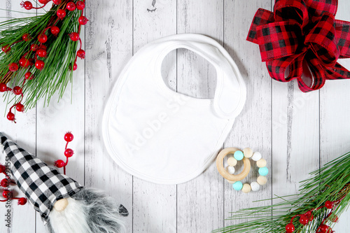 Baby bib product mockup. Christmas farmhouse theme SVG craft product mockup styled with gift with buffalo plaid bow and farmhouse style gnomes against a white wood background.