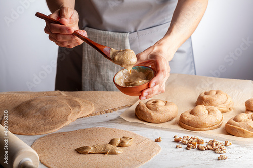 closeup isolated image of a caucasian woman preparing sweet Turkish pastry rolls with tahini and petimezi (tahin pekmez) She mixes the ingredients and spreads it on the flat dough using wooden spoon