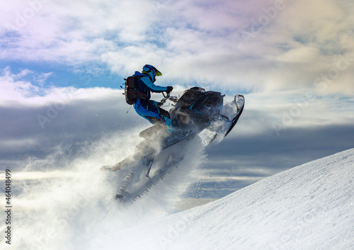 snowmobiler jumps in a bright helmet and overalls over a mountain valley after a snowfall on a frosty morning. snowmobile sports concept