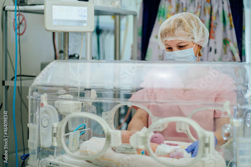 Newborn is placed in the incubator. Neonatal intensive care unit. Female doctor examining newborn baby in incubator. Night shift