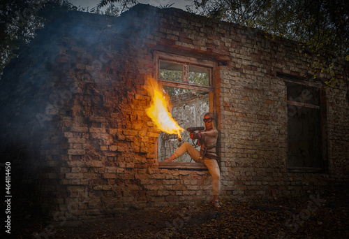 A girl in a military uniform with a flamethrower against the background of an old brick building.