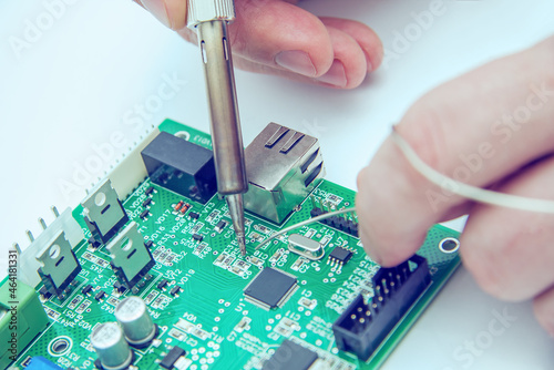 Male hands solder components onto a printed circuit board using copper and a soldering iron. Electronics repair. Selective focus.