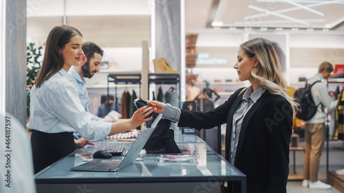 Clothing Store Checkout Cashier Counter: Beautiful Young Woman Buys Blouse from Friendly Retail Sales assistant, Paying with Contactless Credit Card. Fashion Shop with of Designer Brands.