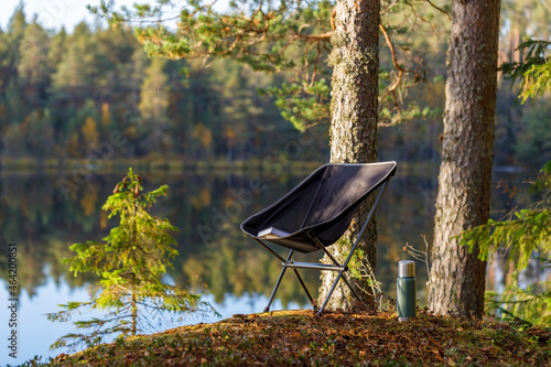 Beautiful forest lake with camping folding chair, book and vacuum insulated bottle.