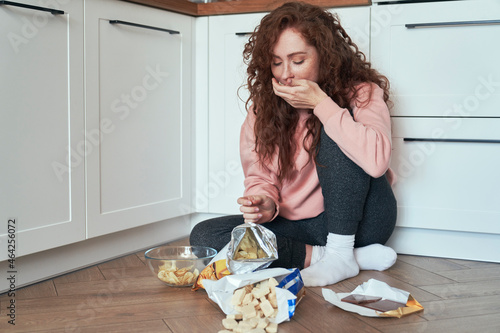 Young caucasian woman having eating disorder and eating greedily on the floor