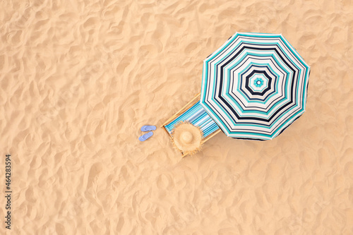 Striped beach umbrella near sunbed with vacationist's stuff on sandy coast, aerial view. Space for text