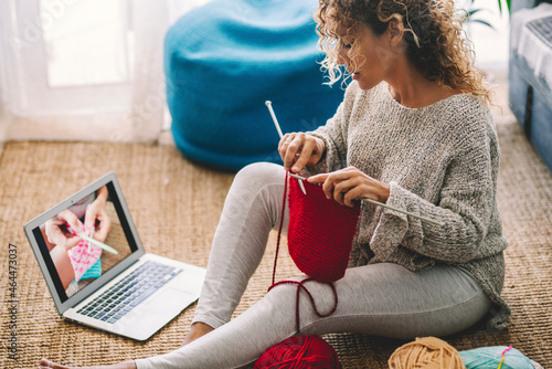 Young woman knitting wool using needle while watching online tutorial on laptop at home. Woman watching needlework lessons, a laptop and home hobbies. Caucasian woman learning to knit online