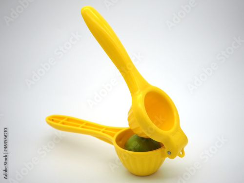 Manual citrus press. Yellow squeezer with green lemon isolated on white background