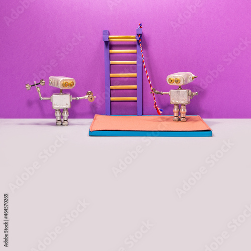 Two robotic athletes in the gym. the first sportsman works with dumbbells, and the second prepares to climb to the top of the wall bars with the help of a rope. Violet gray background