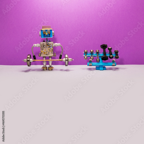A toy robot weightlifter lifts a heavy steel barbell. Rack for barbells and dumbbells of different weights. Violet gray background. Power sport, fitness and weightlifting concept